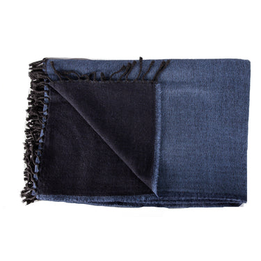 A stack of folded merino wool throws in various solid colors with fringed ends. black navy