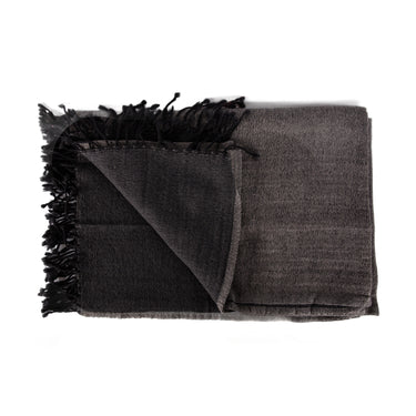 A stack of folded merino wool throws in various solid colors with fringed ends. Merino Boiled Wool Throw grey black