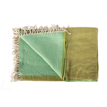 A stack of folded merino wool throws in various solid colors with fringed ends. green aqua