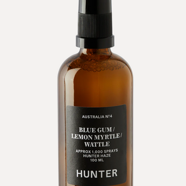 A brown amber glass bottle with a black spray nozzle, labeled 'Hunter' and 'Blue Gum/Lemon Myrtle Wattle' indicating a floral scent, with text stating 'Approx. 1000 sprays' and 'Hunter' branding.