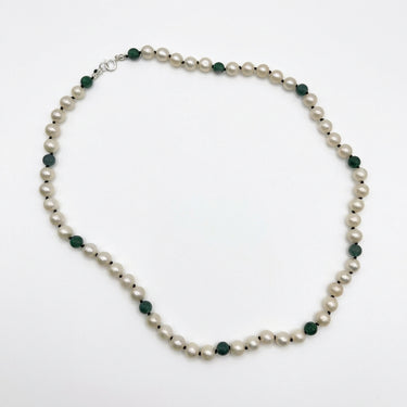 A beaded necklace featuring round off-white pearls separated by small faceted dark green beads, with a silver clasp, displayed on a clean white background.