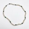 A beaded necklace featuring round off-white pearls separated by small faceted dark green beads, with a silver clasp, displayed on a clean white background.
