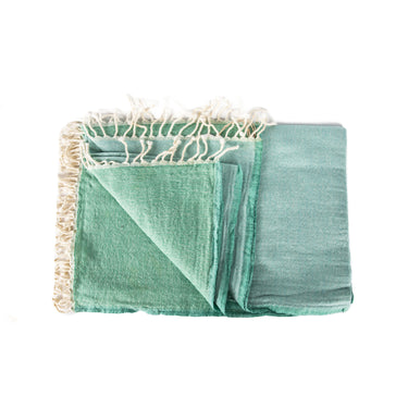 A stack of folded merino wool throws in various solid colors with fringed ends. seafoam