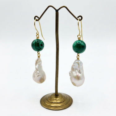 A pair of dangle earrings with gold fishhook clasp, a round dark malachite bead, and a large baroque white pearl drop.
