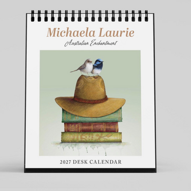 A spiral-bound 2027 desk calendar shown upright on a light gray background. The front cover features the text 'Michaela Laurie Australian Enchantment' above an illustration of a tan hat resting on stacked books, with a small blue-and-white bird perched on top.