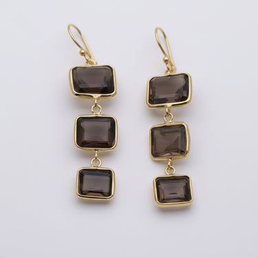 Gold earrings with smoky brown square stones on a marble surface