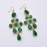 Green teardrop earrings with gold accents on a white stone surface