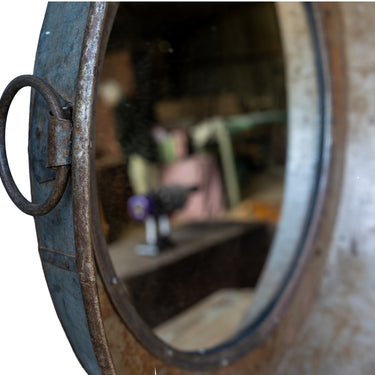 Close-up of a rustic round wall mirror with a thick distressed metal frame and a hanging ring handle 